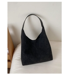 Close-up of black suede hobo bag with smooth leather handles on white bedding backdrop