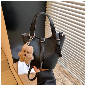Detalle de un bolso cubo negro en cuero con textura de lichi y un colgante de perro suave
