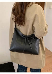 Détail du sac cabas en cuir noir minimaliste avec cordons sur un trench-coat beige