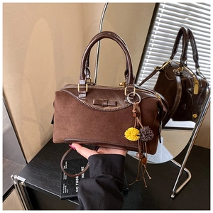 Detail of dark brown suede boston bag with bow accent and fluffy pompom keychain