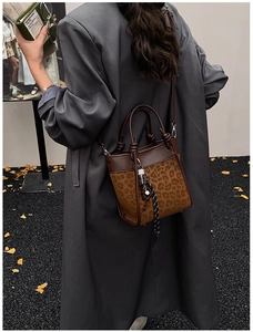 Détail d'un sac seau léopard avec poignées en cuir et breloque décorative pour le style automne