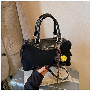 Detail of black leather Boston bag with bow accent and fur charm on a silver suitcase