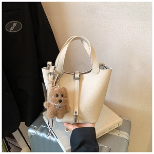 Detalle del bolso de hombro color crema con textura de lichi y colgante de perro de peluche