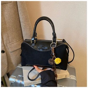 Detail view of black boston bag with bow accent, fur charms, and dual texture finish