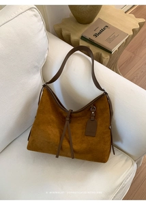 Gros plan du sac hobo en daim marron avec bandoulière en cuir sur un canapé blanc