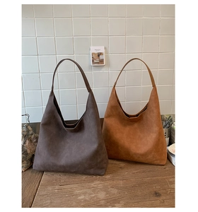 Detail of minimalist suede hobo bags in dark brown and caramel on a wooden surface