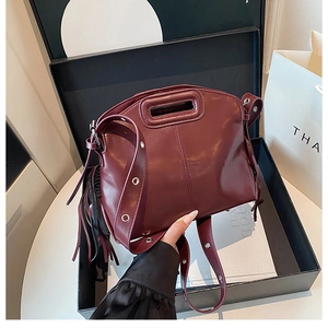 Detailed close-up of a burgundy leather handbag featuring unique fringe and wide strap