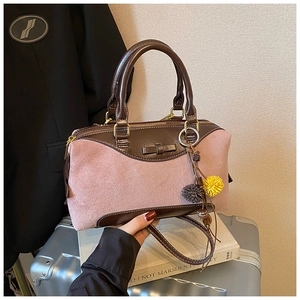 Detailed shot of pink suede Boston bag with brown leather trim and charms on a suitcase