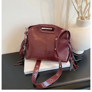 Detail view of burgundy leather handbag with long tassels and silver grommet shoulder strap
