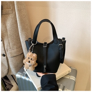 Detalle del bolso de cuero negro con grano de lichi y colgante de perro de peluche marrón