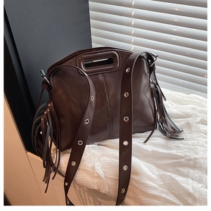 Close-up of dark brown handbag featuring long side fringes and decorative metal eyelets
