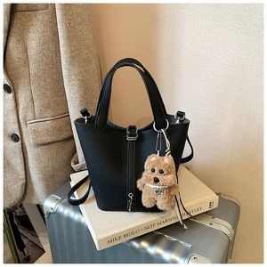 Detalle de bolso bucket de cuero granulado negro con cierre metálico y osito de peluche
