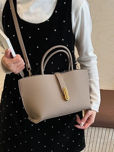 Taupe pebbled leather bucket bag with top handles and gold hardware worn by a model