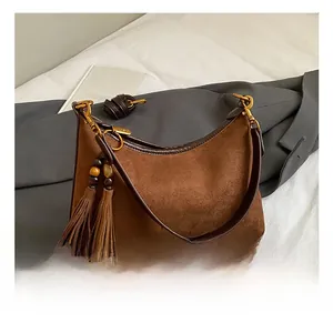 Detail of brown suede handbag featuring fringe tassels, wooden beads and gold hardware