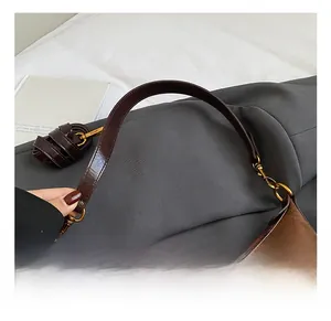 Close-up of brown baguette bag featuring a dark leather handle and gold metal hardware