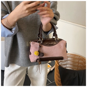 Detail of pink and brown suede Boston bag with fuzzy pompom charm and leather handle