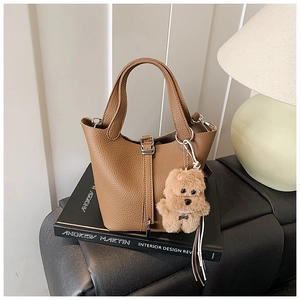 Detalle del bolso de cubo en cuero marrón con patrón litchi y colgante de felpa suave