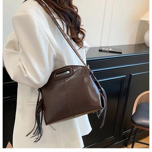 Detailed view of deep brown glossy leather handbag featuring long fringe side tassels