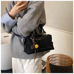 Detail of black suede Boston bag with colorful pom-pom charms and golden hardware