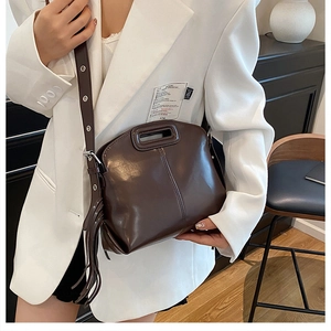 Close-up of a dark brown glossy leather bag with adjustable strap and side tassel detail