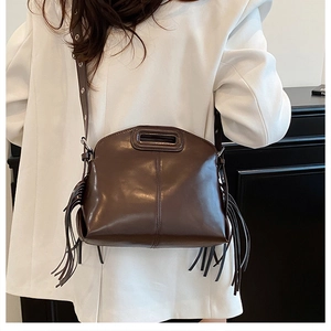 Detail of dark brown leather crossbody bag with fringe accents and curved design