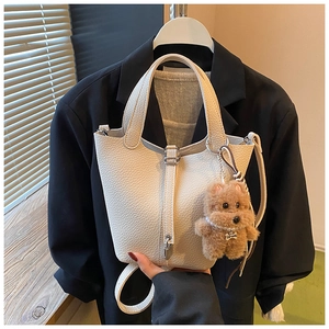 Detalle del bolso de cubo crema con textura de lichi y colgante de perro de peluche