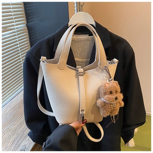 Detalle del bolso tipo cubo beige con textura de lichi y un tierno colgante de osito