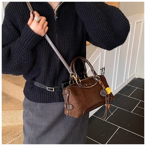 Detail of a brown suede Boston bag with leather bow and tassel charm on model