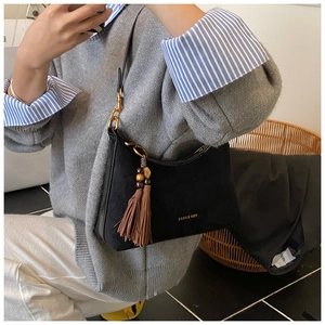 Detail of black suede baguette bag with gold metal hardware and boho tassel charm