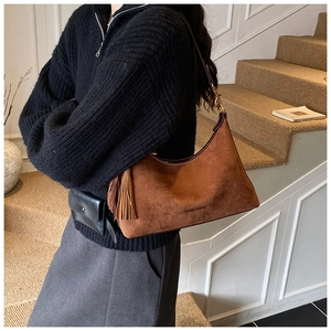 Brown suede hobo bag with long tassels shown on shoulder in a lifestyle setting