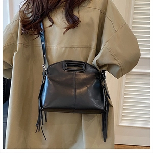 Detail of a black leather handbag with side tassels and unique cutout handle worn with outfit