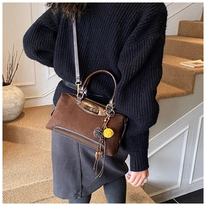 Detail of dark brown suede Boston bag with leather handles and furry ball charm accessory