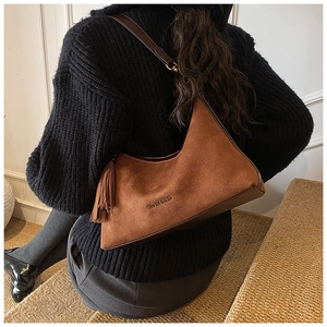 Detail showing brown suede baguette bag with tassel and logo worn by model in black sweater