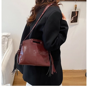 Detail view of wine red leather handbag featuring long fringe and cutout handle