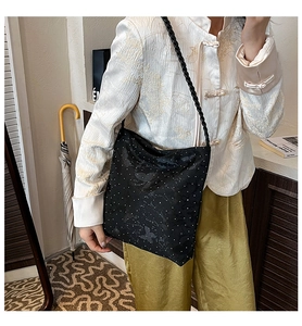 Fashionable black shoulder bag with polka dots and butterfly patterns worn by a model