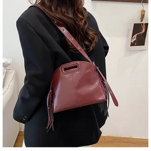 Detail of burgundy leather crossbody bag featuring fringe accents and eyelet wide strap