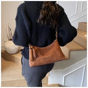 Close-up of brown suede saddle bag with fringe tassel and adjustable shoulder strap