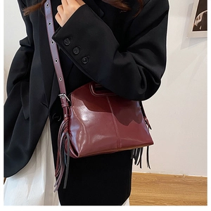 Detail view of burgundy leather handbag featuring long fashion fringe and wide shoulder strap