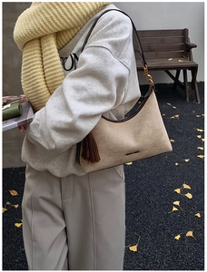 Detail of beige suede baguette bag with leather straps and decorative tassel charm
