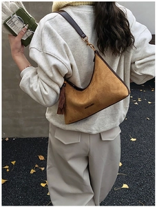 Close-up of a dark brown suede hobo bag with fringe detail and a leather shoulder strap
