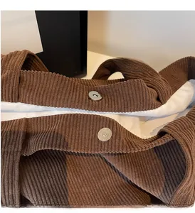 Detail of silver magnetic snap closure on brown corduroy tote bag with white lining