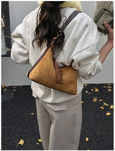Detail of camel suede baguette bag with leather strap and fringe on autumn street