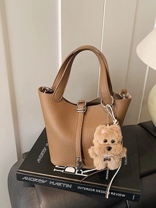 Bolso tipo cubo de cuero marrón con grano, cierre plateado y colgante de perro de peluche
