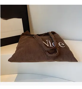 Detailed view of brown corduroy tote bag featuring white embroidered Nice letter text