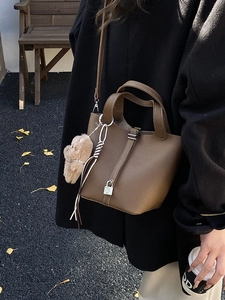 Bolso cubo de cuero marrón oscuro con patrón lichi, cierre metálico y colgante de oso