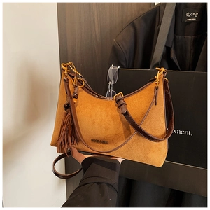 Detailed shot of brown suede baguette bag with tassel detail and metal logo accent