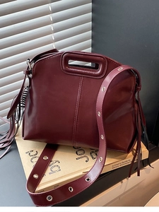 Dark red leather crossbody handbag with tassel details and hollow handle on display