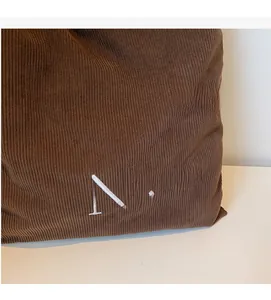 Detailed view of brown corduroy fabric and white Nice embroidery on the tote bag