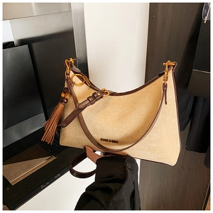 Close-up of suede baguette bag with leather trim and decorative fringe detail