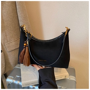 Close-up of black suede baguette bag with gold logo and stylish tassel detail